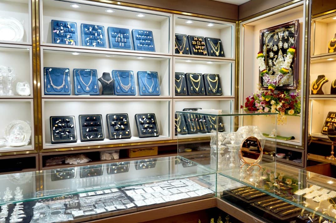 Inside Shree Ashhtalaxmi Jewellers showroom: gold-trimmed shelves with necklaces and rings on velvet display trays